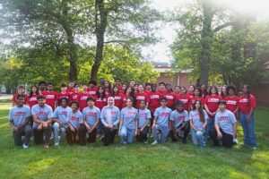 A group of young people wearing STEM Ambassador shirts pose in a grassy area